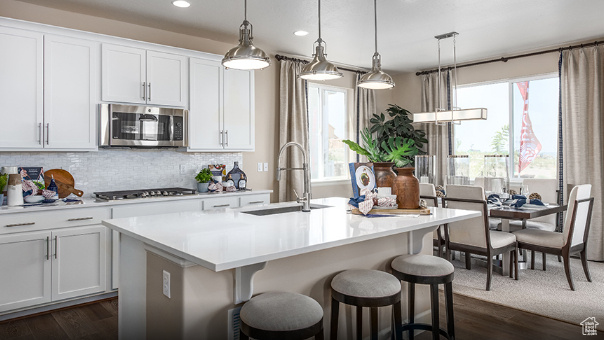 Kitchen with stainless steel microwave, gas cooktop, recessed lighting, a center island with sink, and light countertops