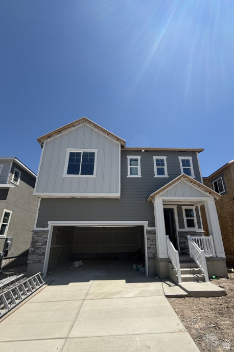 View of front of home with a garage, board and batten siding, concrete driveway, and stone siding