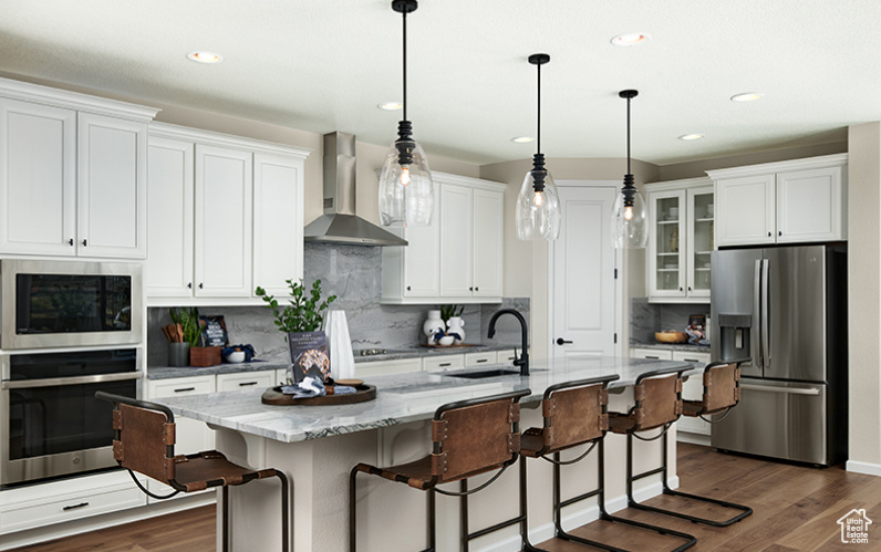 Kitchen featuring appliances with stainless steel finishes, wall chimney range hood, a sink, dark wood finished floors, and white cabinetry