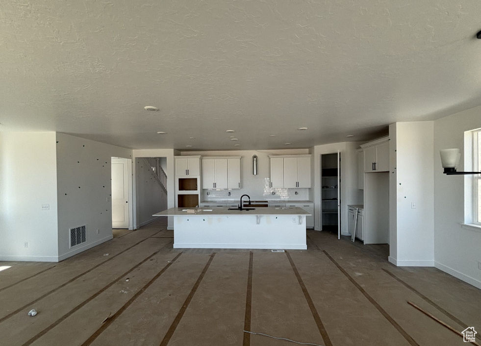 Kitchen featuring a center island with sink, white cabinets, and a textured ceiling