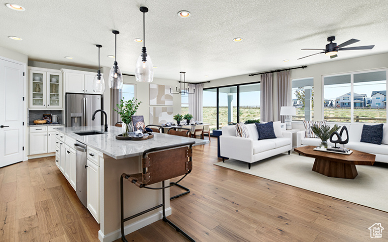Kitchen featuring a sink, open floor plan, stainless steel appliances, a textured ceiling, and white cabinetry