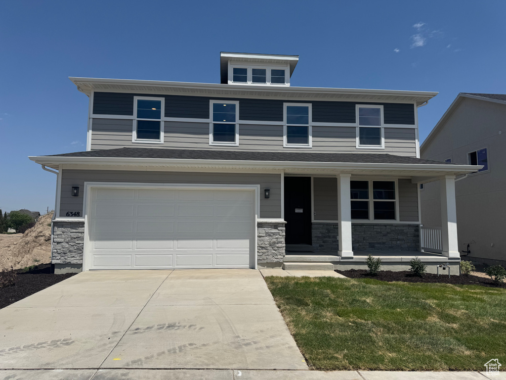 American foursquare style home with driveway, a garage, stone siding, covered porch, and a front yard