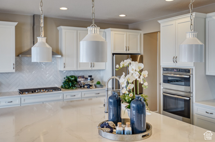 Kitchen featuring stainless steel double oven, wall chimney range hood, black cooktop, white cabinets, and backsplash