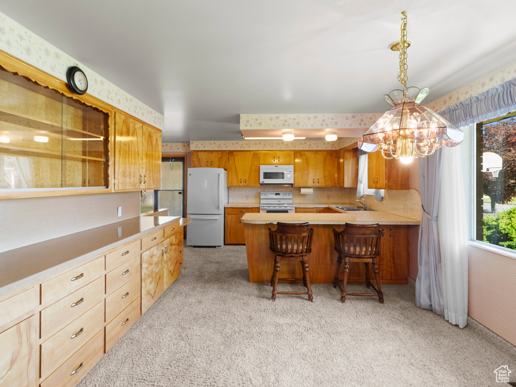Kitchen featuring white appliances, light colored carpet, a chandelier, and light countertops