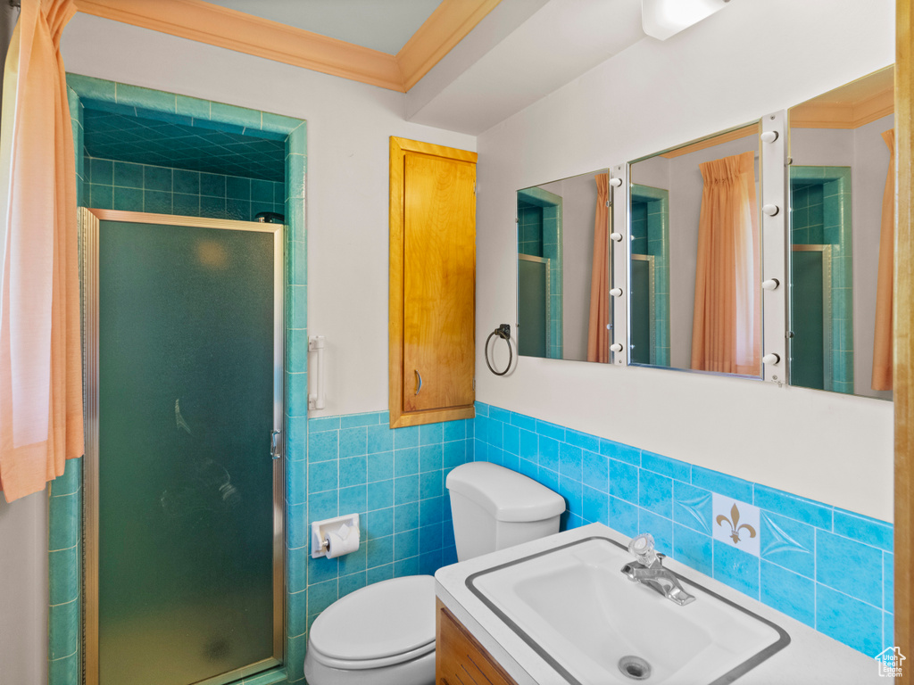Full bathroom featuring tile walls, a shower stall, toilet, vanity, and wainscoting