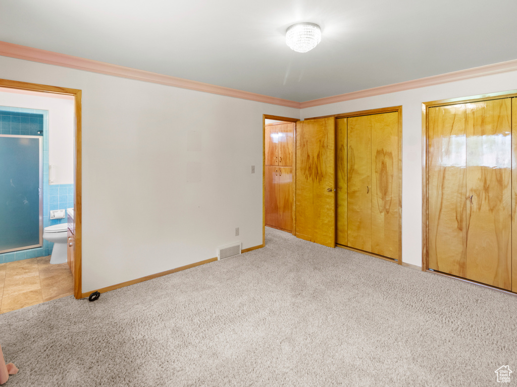 Unfurnished bedroom with carpet flooring, two closets, ornamental molding, ensuite bathroom, and baseboards