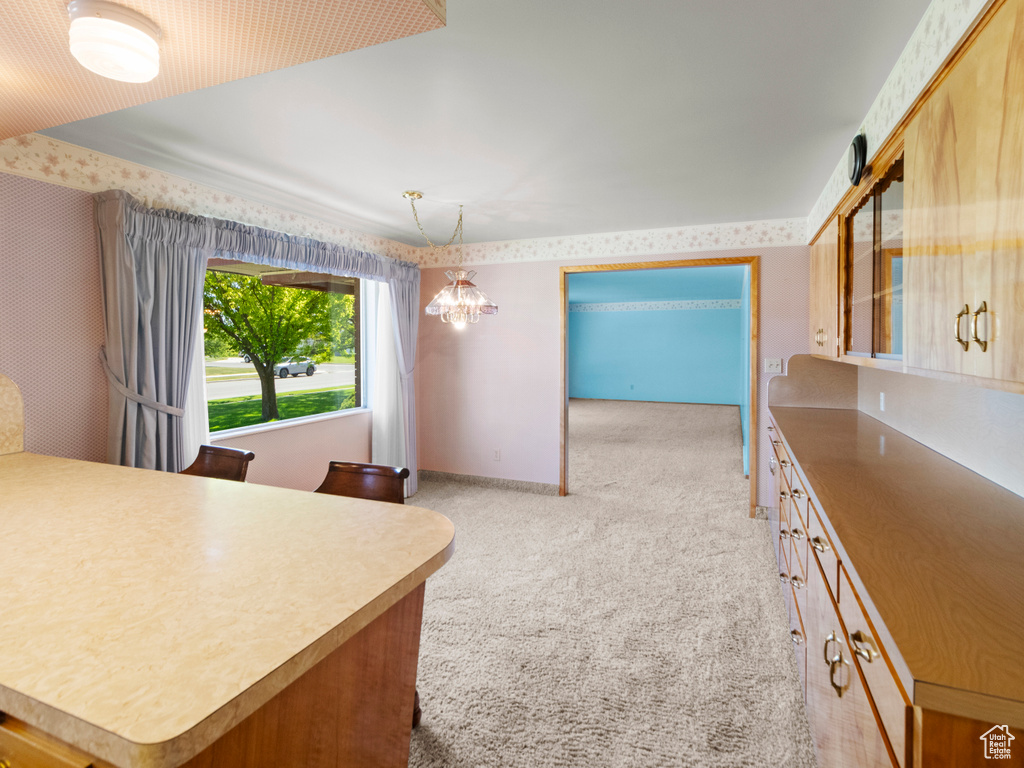Kitchen with light carpet, a chandelier, wallpapered walls, and decorative light fixtures