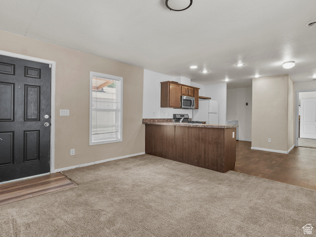Kitchen with appliances with stainless steel finishes, a peninsula, dark carpet, and baseboards