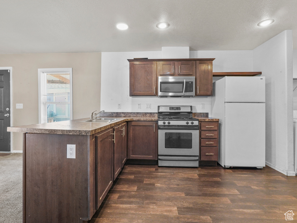 Kitchen with stainless steel appliances, a sink, a peninsula, dark wood-style floors, and dark brown cabinets