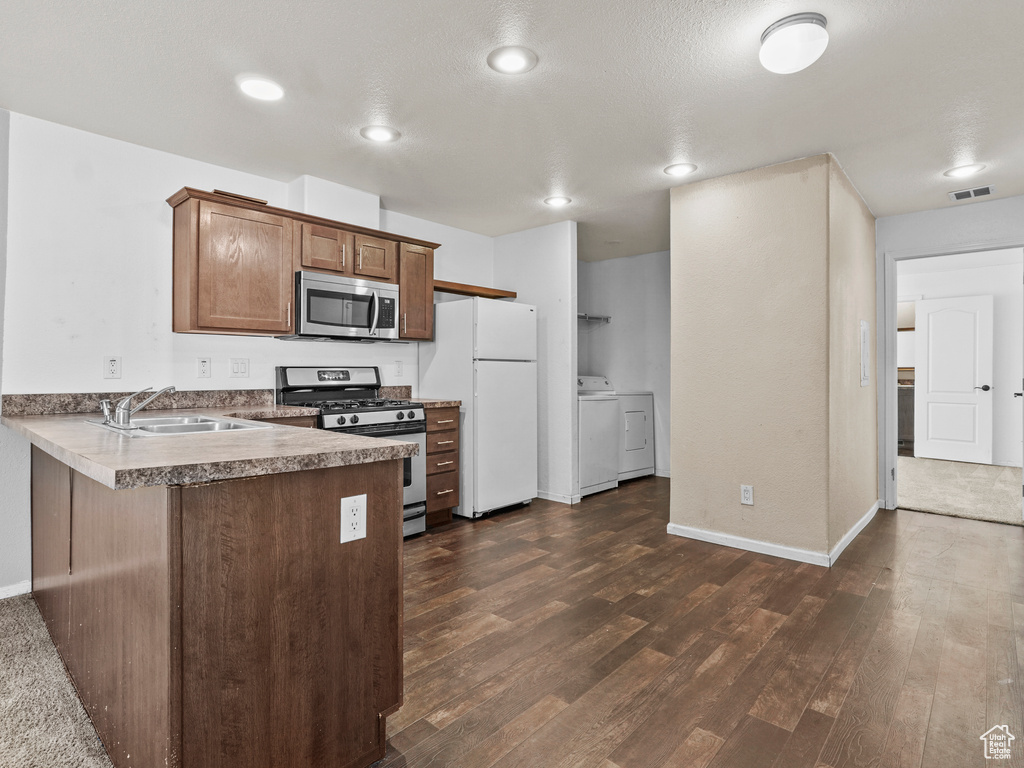 Kitchen with appliances with stainless steel finishes, a sink, dark wood-type flooring, a peninsula, and baseboards