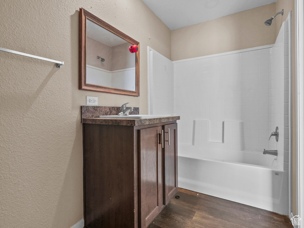 Bathroom featuring a textured wall, wood finished floors, vanity, and bathtub / shower combination