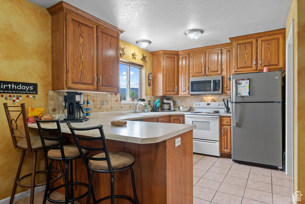 Kitchen with decorative backsplash, stainless steel appliances, light countertops, brown cabinets, and a peninsula