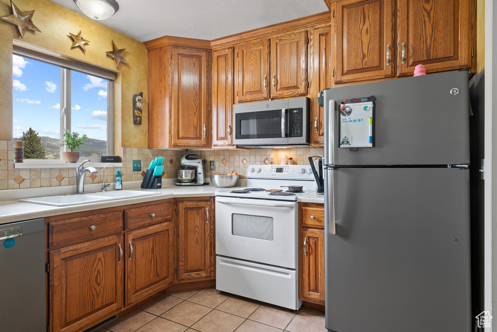 Kitchen with brown cabinets, stainless steel appliances, light countertops, and a sink