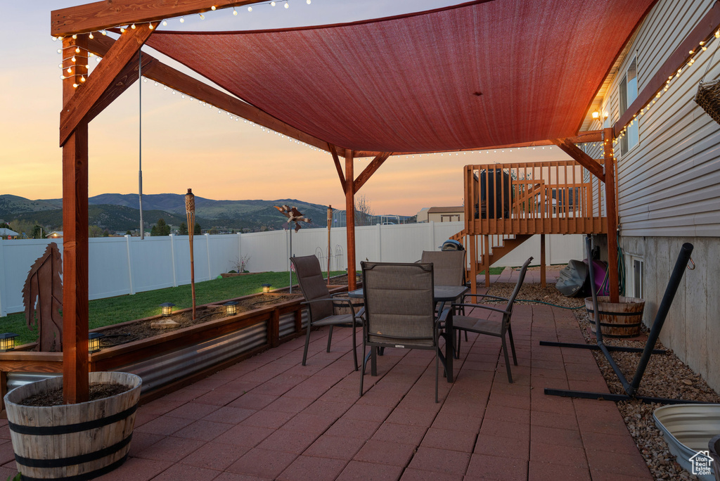 Patio terrace at dusk featuring stairs, outdoor dining space, a lawn, a deck with mountain view, and a fenced backyard