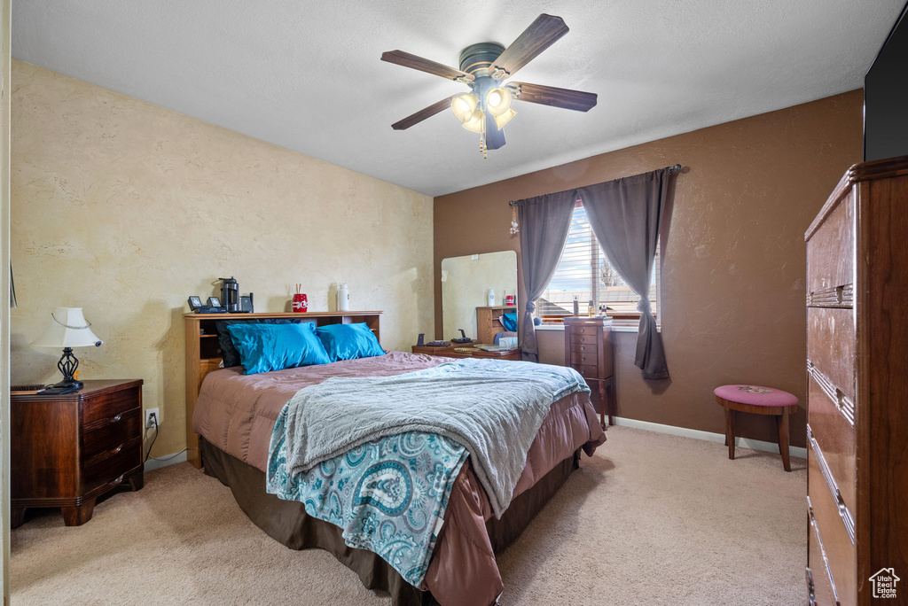 Carpeted bedroom featuring a textured wall, ceiling fan, and baseboards