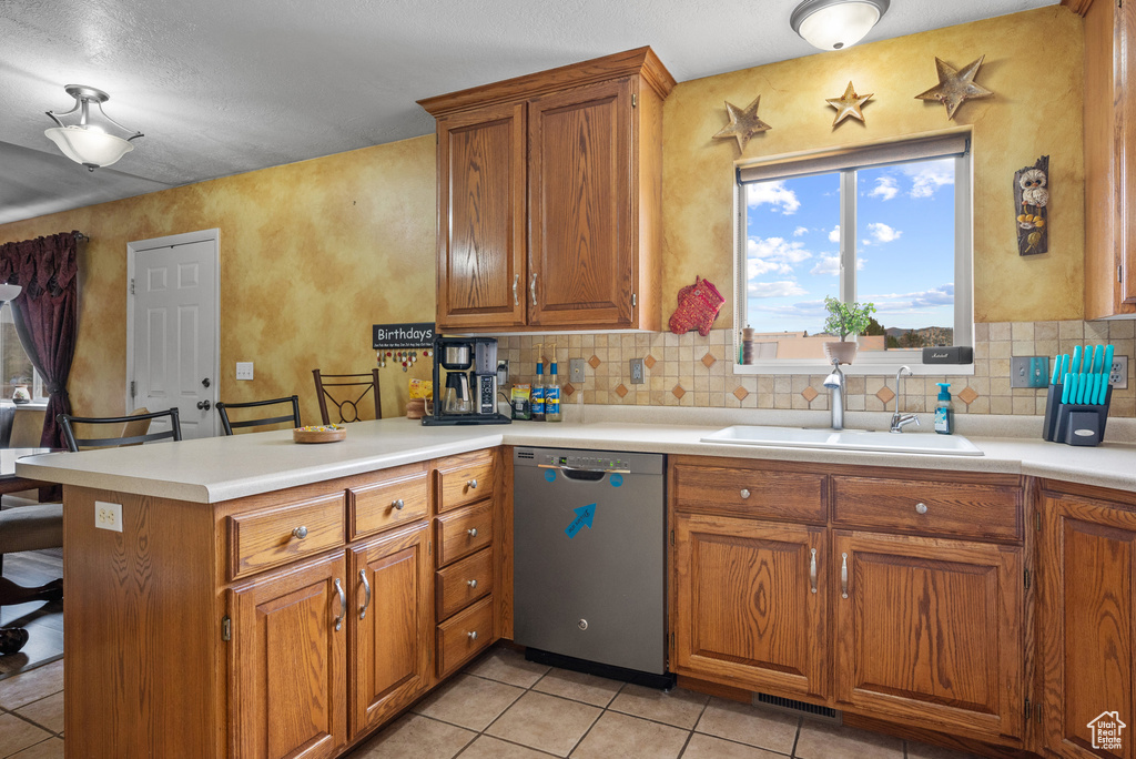 Kitchen featuring stainless steel dishwasher, decorative backsplash, brown cabinetry, a sink, and a peninsula