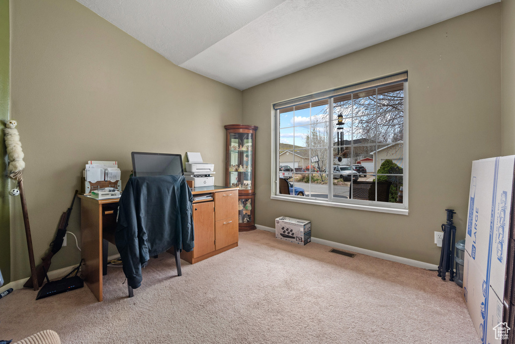 Office with lofted ceiling, visible vents, baseboards, and light carpet