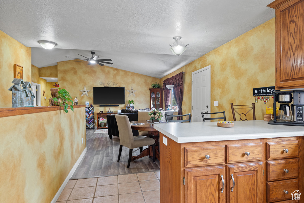 Kitchen with light tile patterned floors, ceiling fan, brown cabinetry, vaulted ceiling, and light countertops