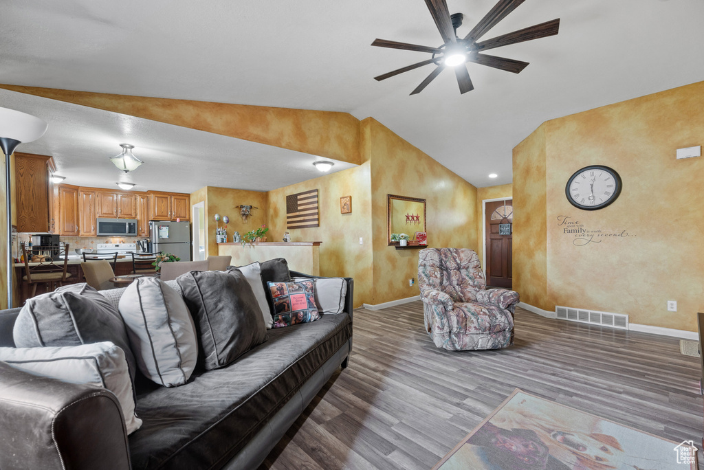 Living room featuring wood finished floors, vaulted ceiling, ceiling fan, baseboards, and visible vents