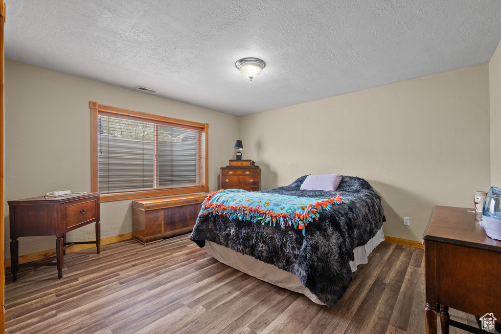 Bedroom with baseboards, visible vents, wood finished floors, and a textured ceiling