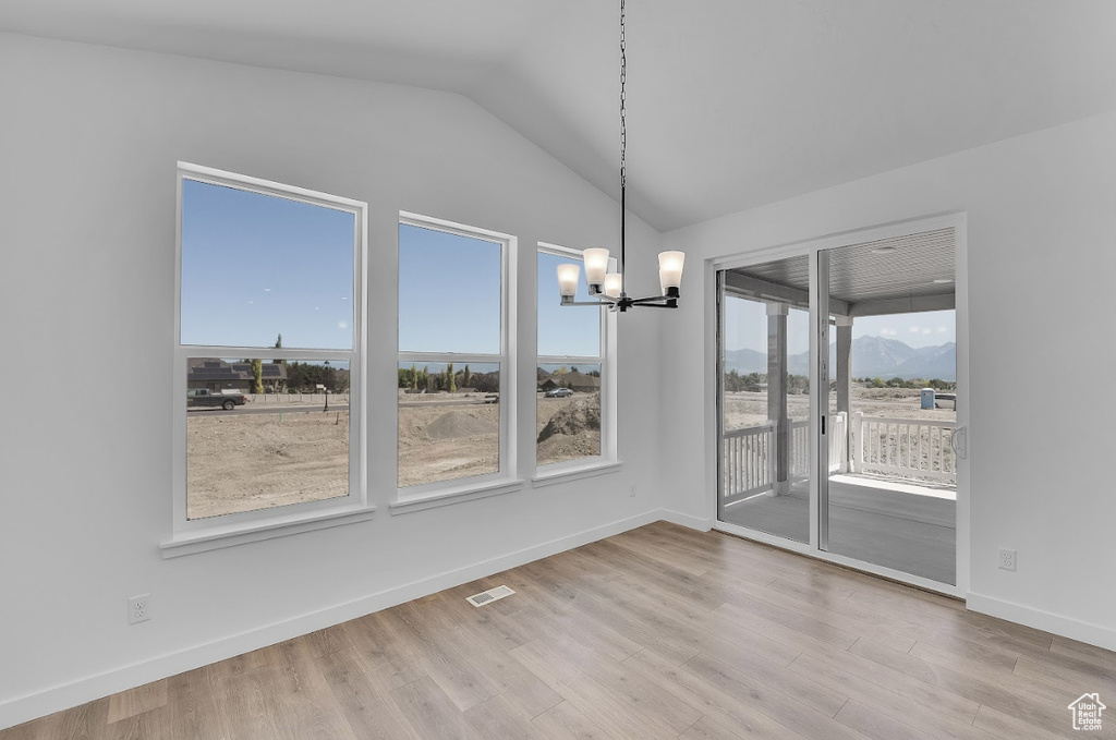 Unfurnished dining area featuring a chandelier, lofted ceiling, wood finished floors, and a mountain view