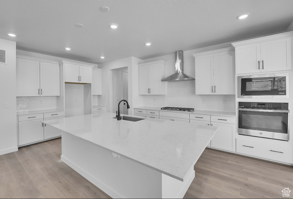 Kitchen with appliances with stainless steel finishes, wall chimney range hood, a large island with sink, white cabinets, and recessed lighting