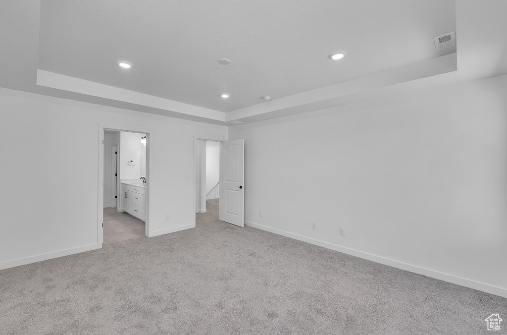 Unfurnished bedroom featuring a raised ceiling, recessed lighting, and light carpet