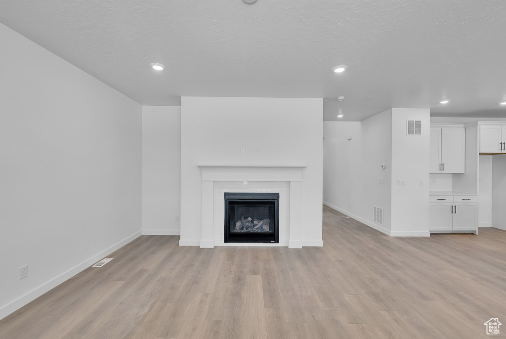 Unfurnished living room featuring light wood-type flooring, recessed lighting, and a glass covered fireplace