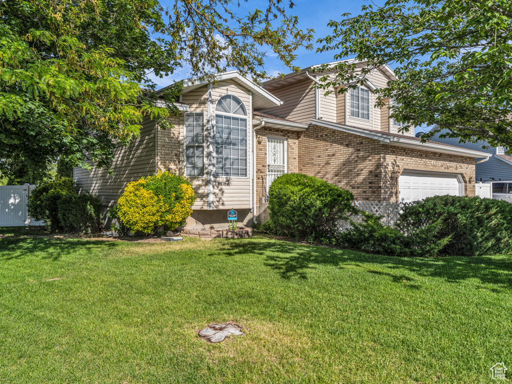 View of front facade with a front yard, brick siding, and a garage