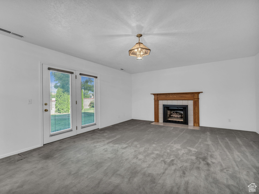 Unfurnished living room featuring carpet floors, a tile fireplace, and a textured ceiling