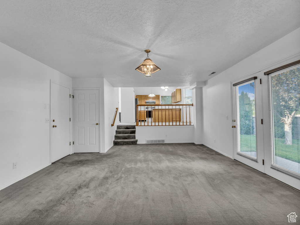 Unfurnished living room with carpet floors, stairs, a textured ceiling, and baseboards