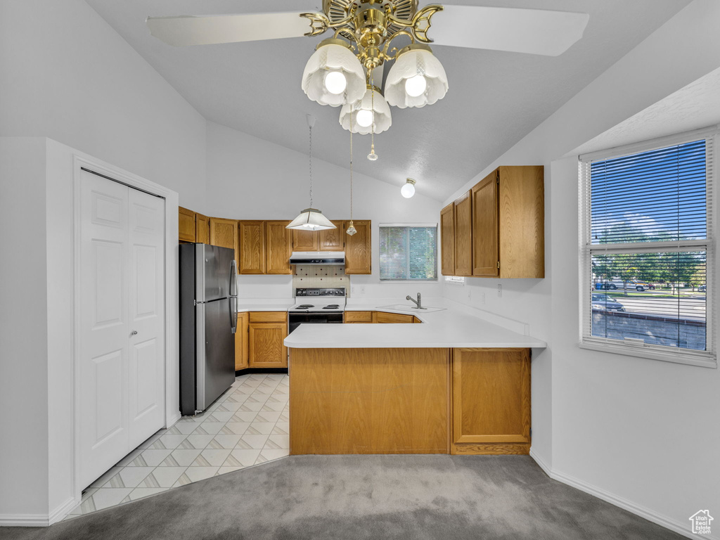 Kitchen featuring freestanding refrigerator, range with electric stovetop, a sink, brown cabinetry, and a peninsula