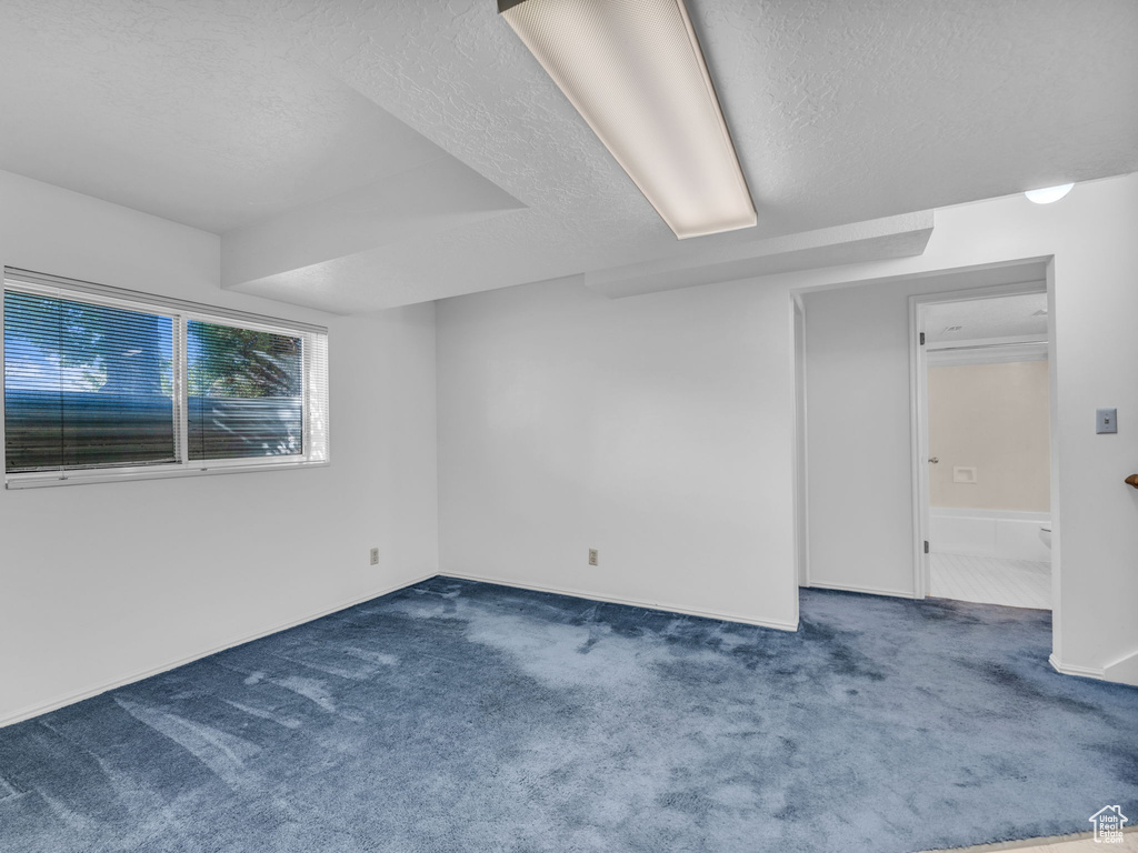 Carpeted empty room with a textured ceiling and baseboards