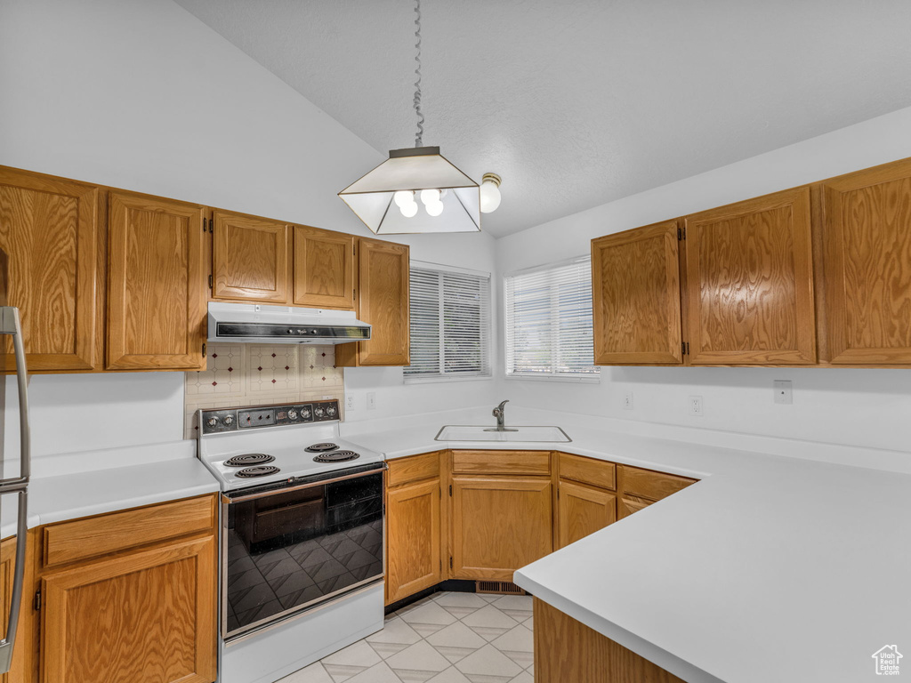 Kitchen featuring electric stove, a sink, under cabinet range hood, vaulted ceiling, and light countertops