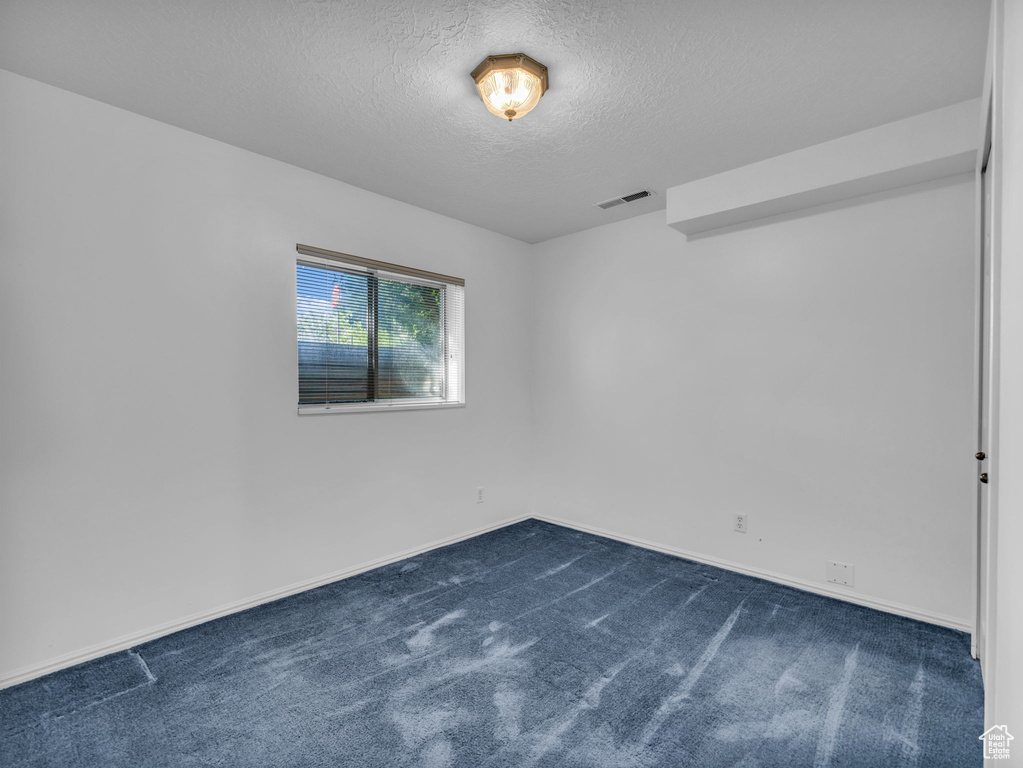 Empty room featuring a textured ceiling, dark carpet, and baseboards