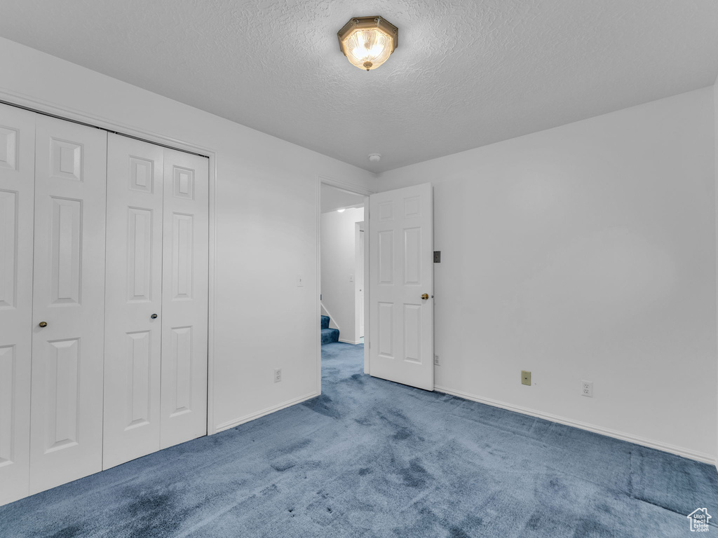 Unfurnished bedroom featuring a textured ceiling, carpet flooring, baseboards, and a closet