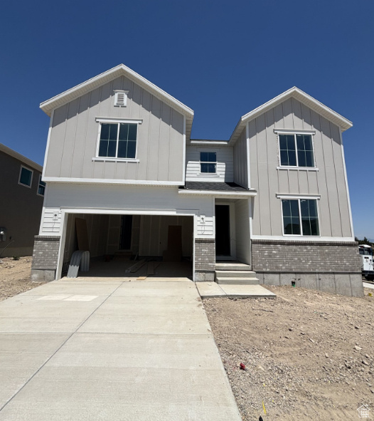 View of front of house with brick siding, a garage, board and batten siding, and driveway