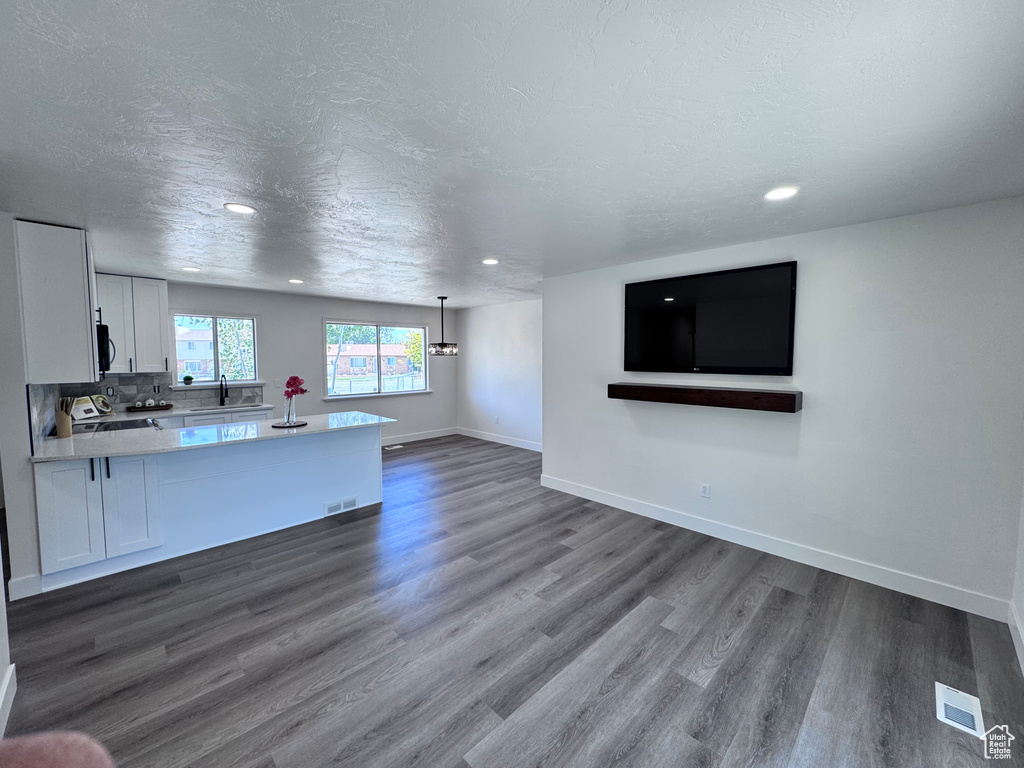Unfurnished living room with a sink, dark wood finished floors, baseboards, recessed lighting, and a textured ceiling