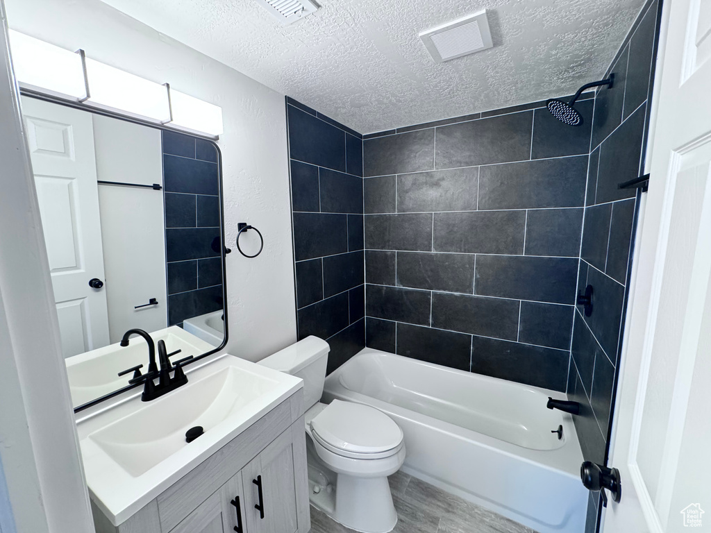 Bathroom featuring a textured ceiling, vanity, toilet, shower / tub combination, and wood finished floors