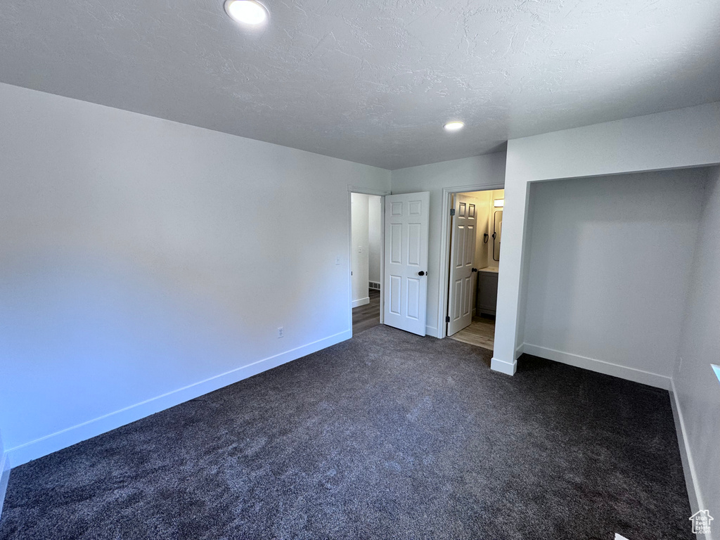 Unfurnished bedroom featuring baseboards, dark colored carpet, recessed lighting, a textured ceiling, and connected bathroom