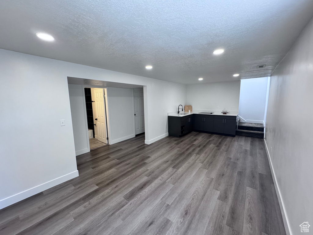 Finished basement featuring baseboards, a textured ceiling, recessed lighting, wet bar, and dark wood finished floors