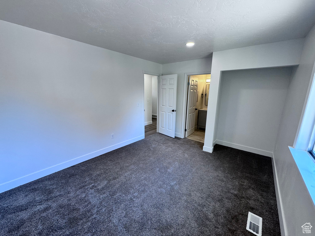 Unfurnished bedroom featuring dark carpet, baseboards, a textured ceiling, and ensuite bathroom
