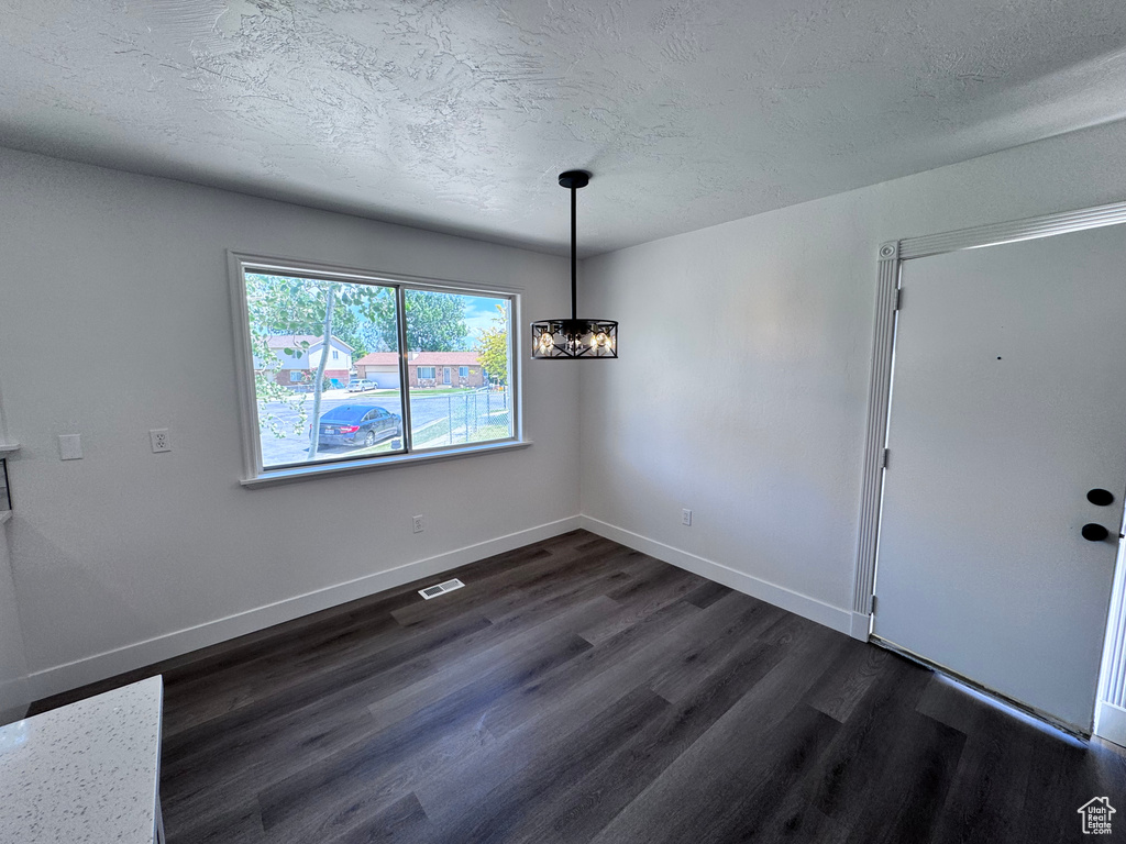 Unfurnished dining area with dark wood-style floors, a textured ceiling, and baseboards