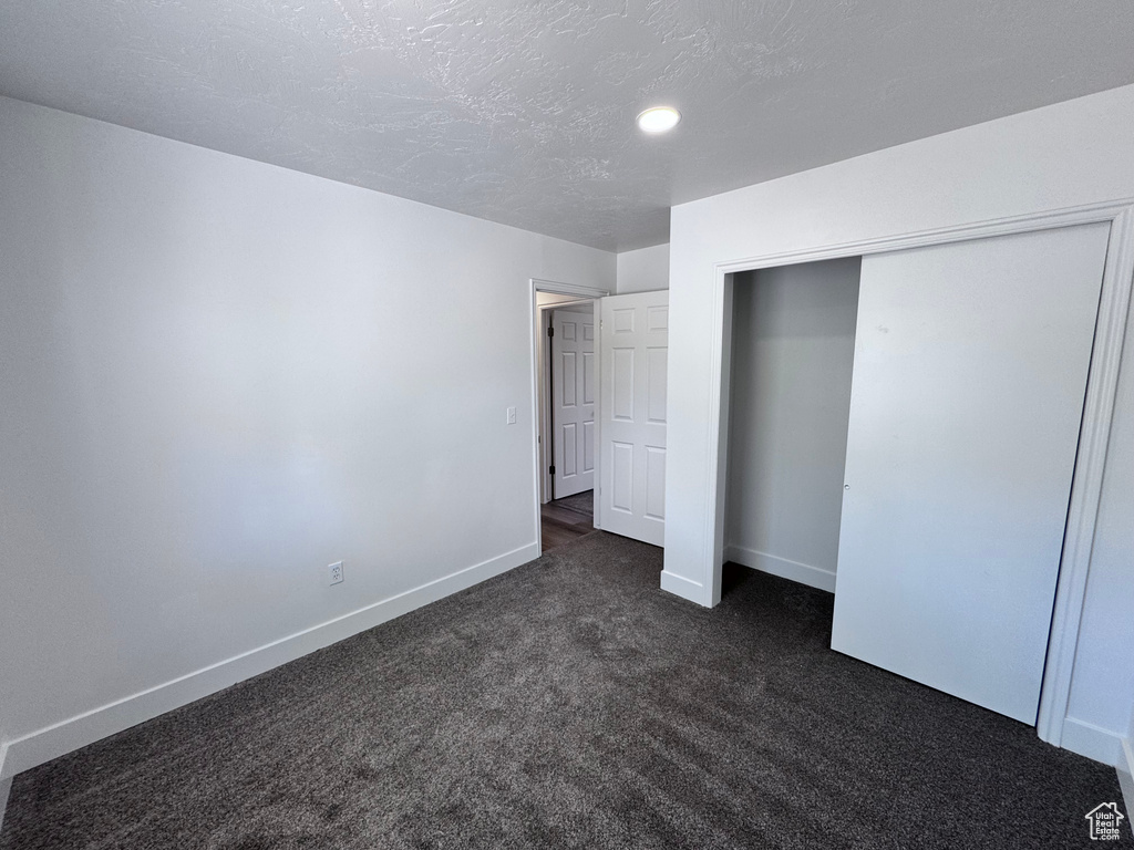 Unfurnished bedroom with baseboards, dark colored carpet, a closet, and a textured ceiling