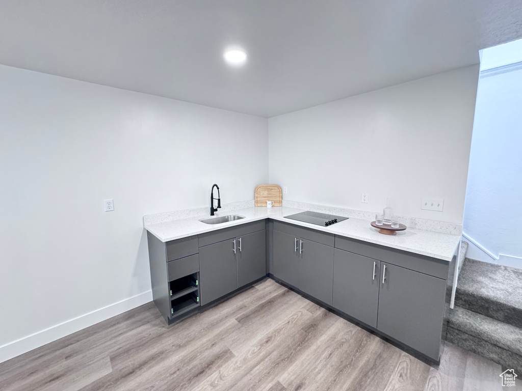 Kitchen with gray cabinetry, a sink, light wood-type flooring, and light countertops