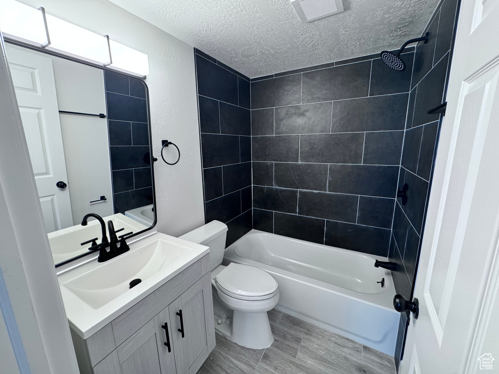 Full bath with a textured ceiling, vanity, toilet, and shower / tub combination