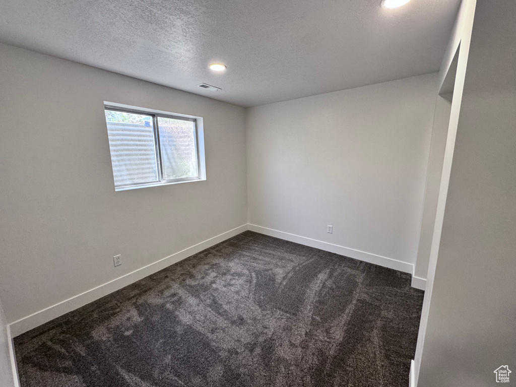 Unfurnished room featuring dark carpet, a textured ceiling, and baseboards