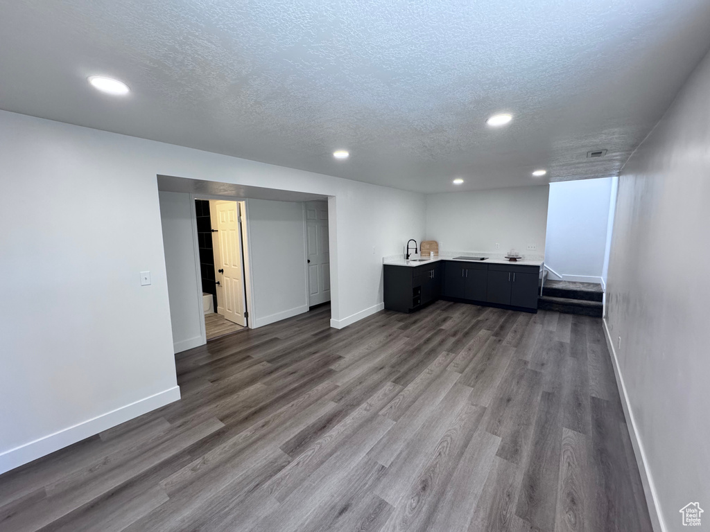 Below grade area featuring a textured ceiling, recessed lighting, bar with sink, baseboards, and dark wood finished floors