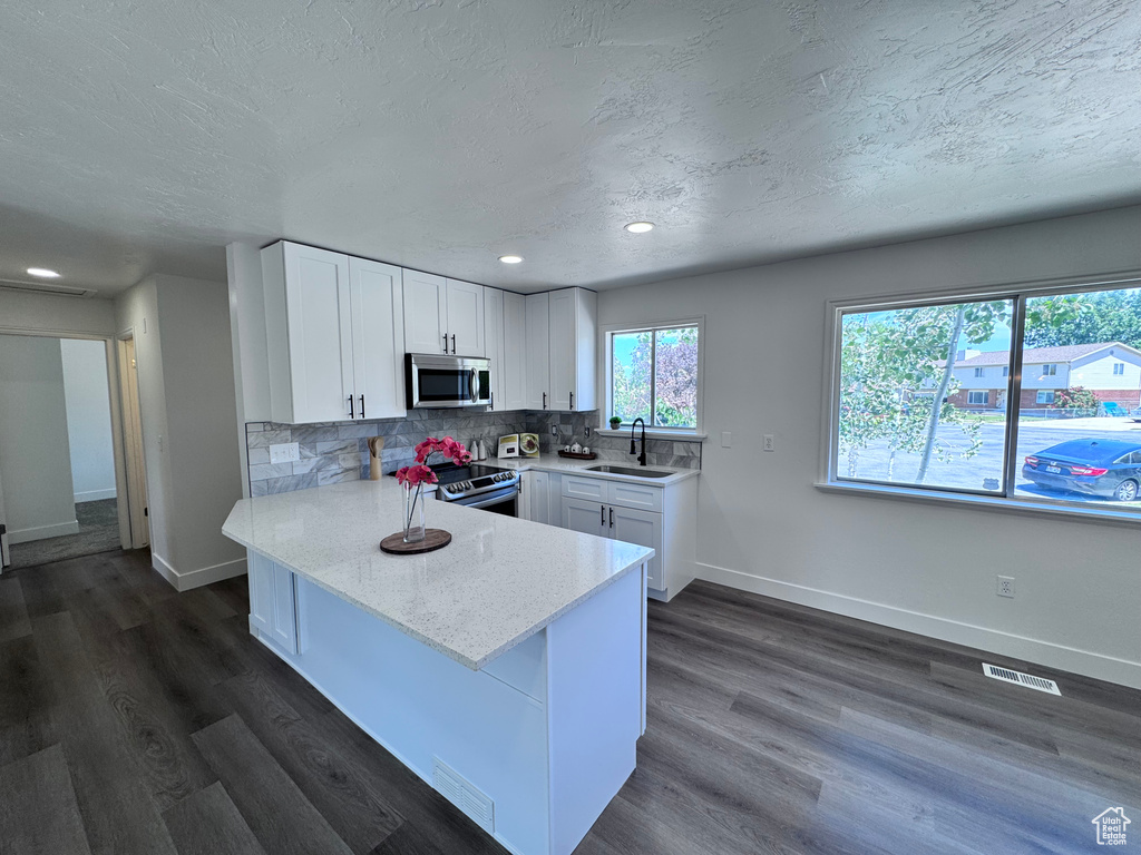 Kitchen with stainless steel appliances, white cabinets, baseboards, a peninsula, and a textured ceiling