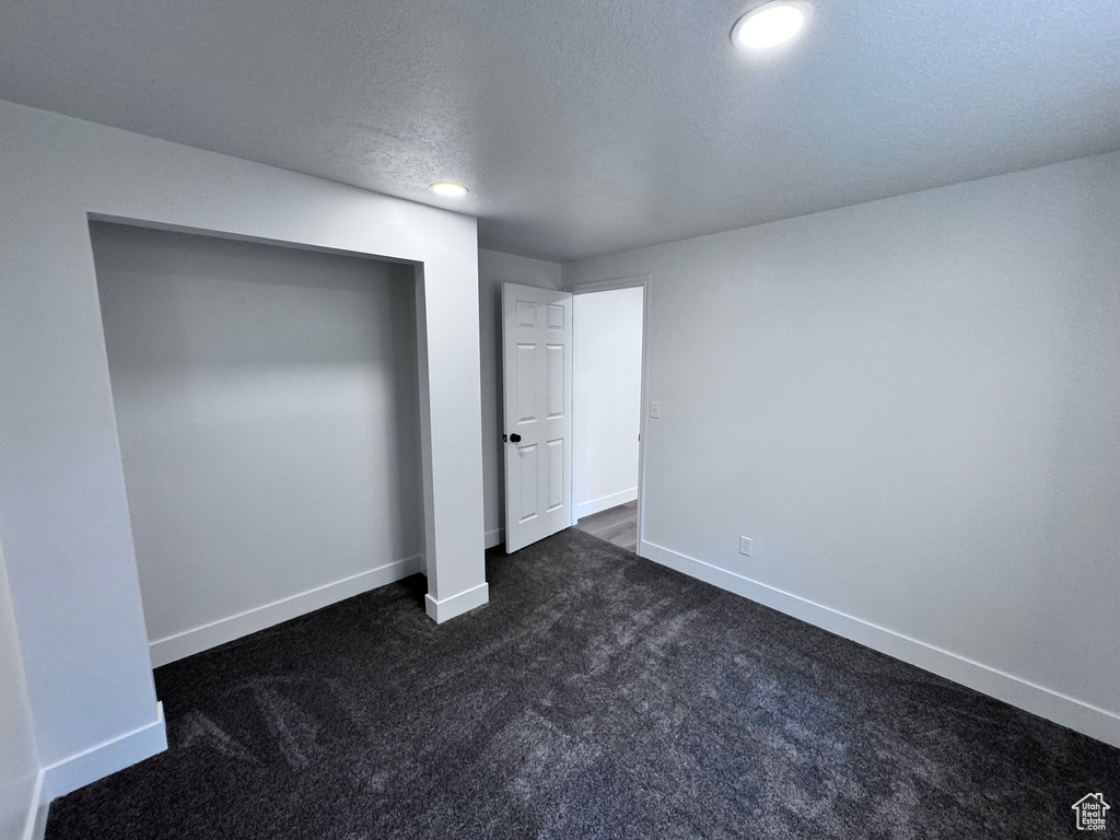 Unfurnished bedroom featuring dark carpet, baseboards, recessed lighting, a textured ceiling, and a closet